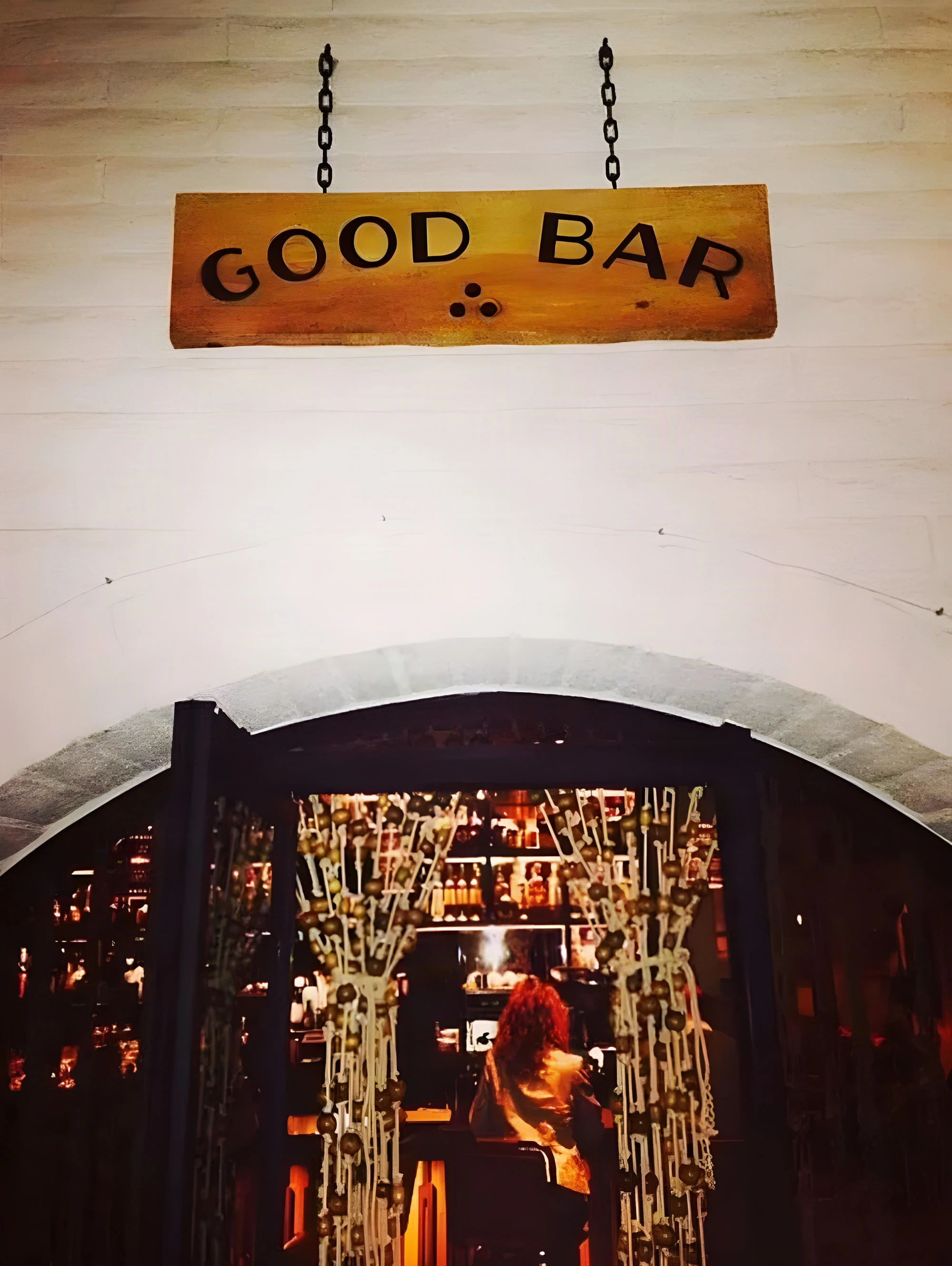 Hanging Good Bar sign above an arched doorway with a beaded curtain