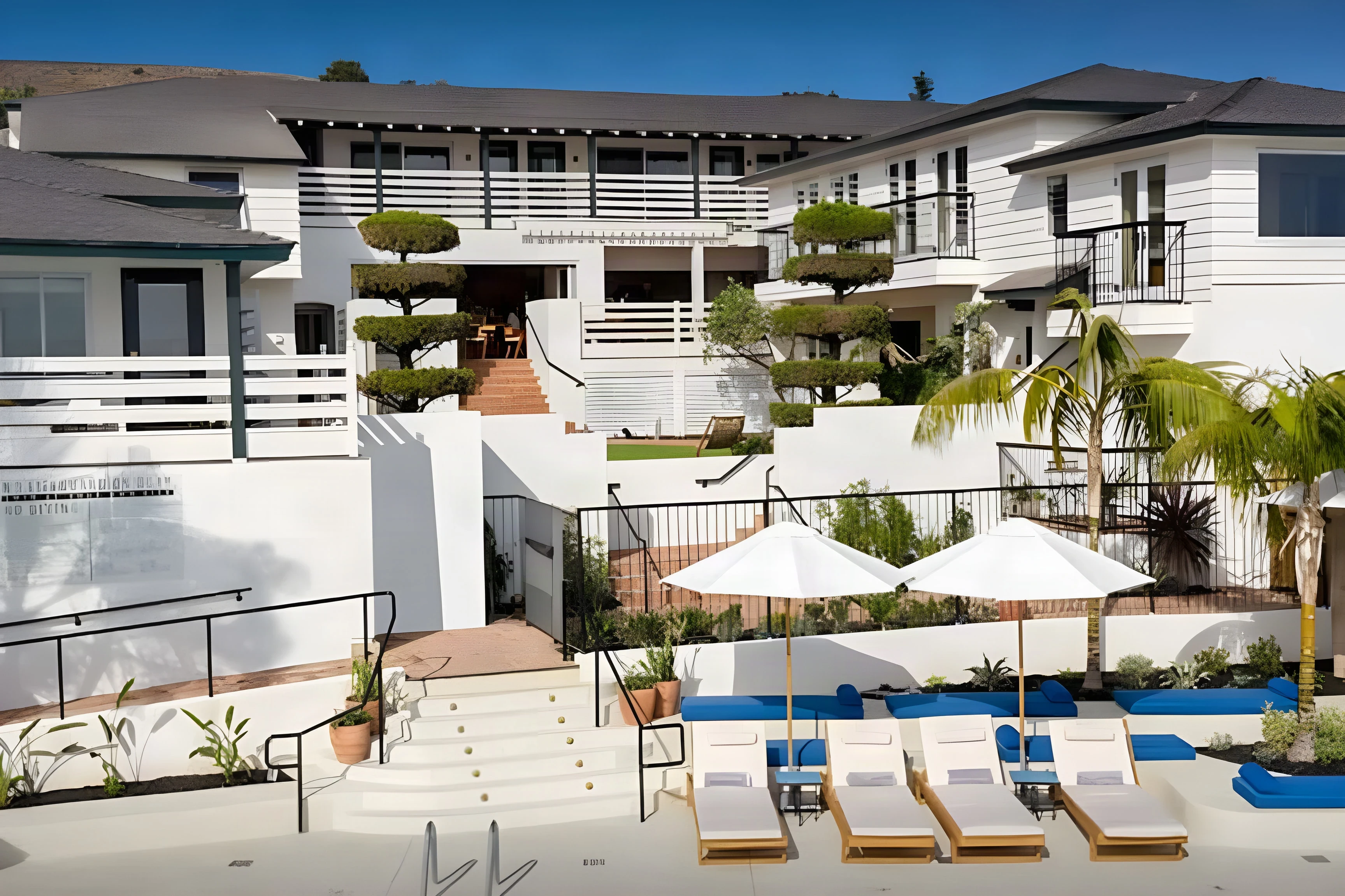 White Laguna Beach hotel above a pool terrace with blue umbrellas and loungers