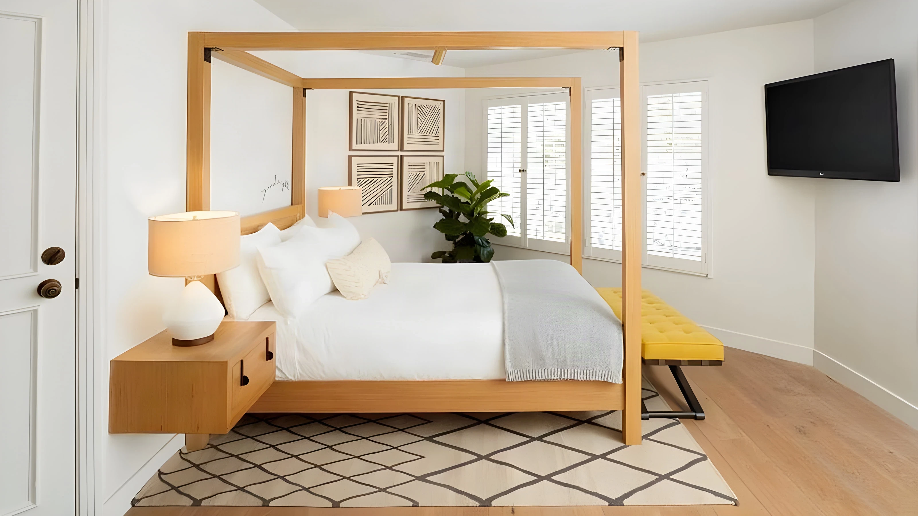 Canopy bed in pale oak with a yellow bench and framed prints in a Landsby guest room