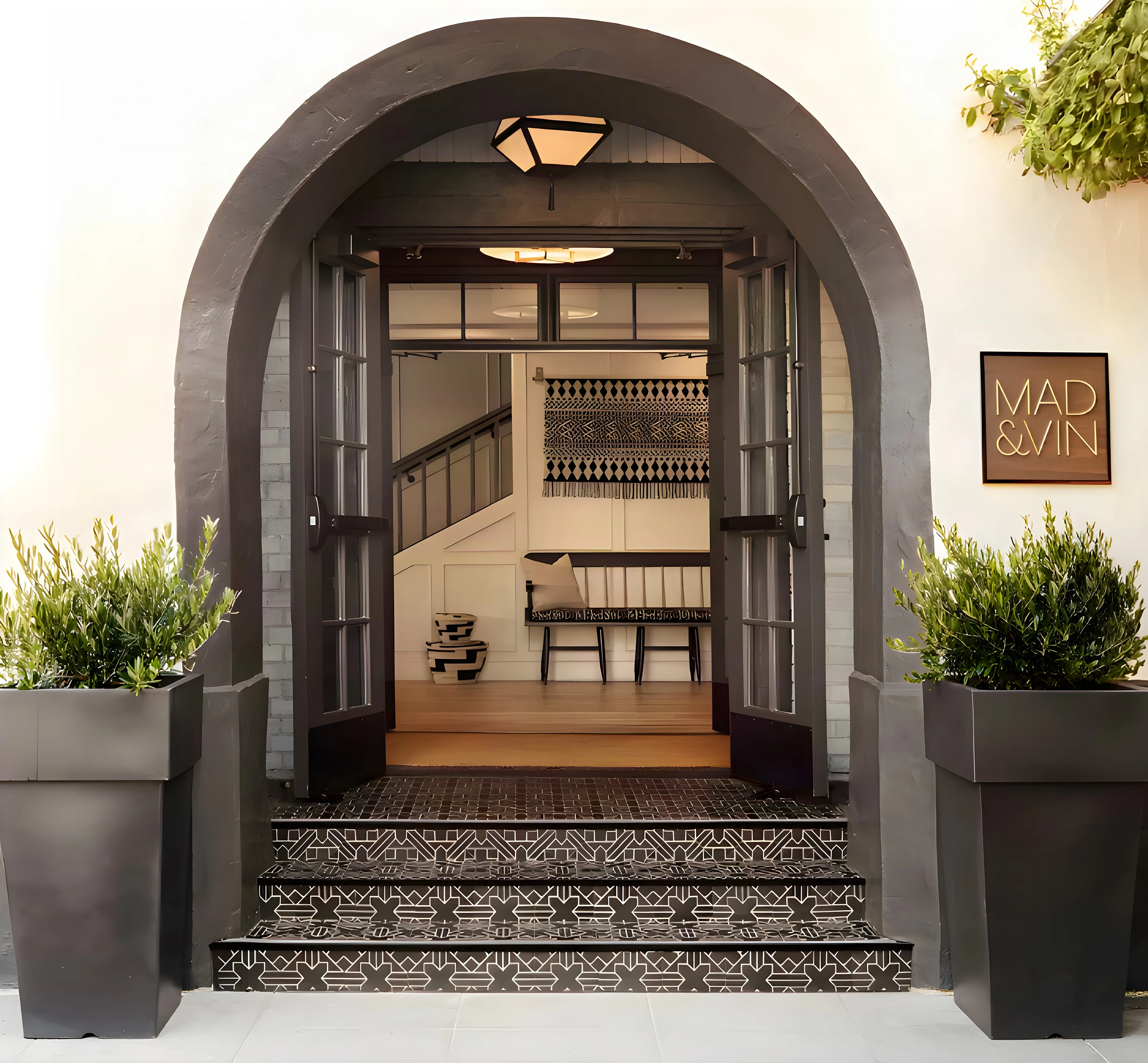Mad & Vin arched black front door in Solvang with patterned tile steps, potted olive trees and the restaurant sign