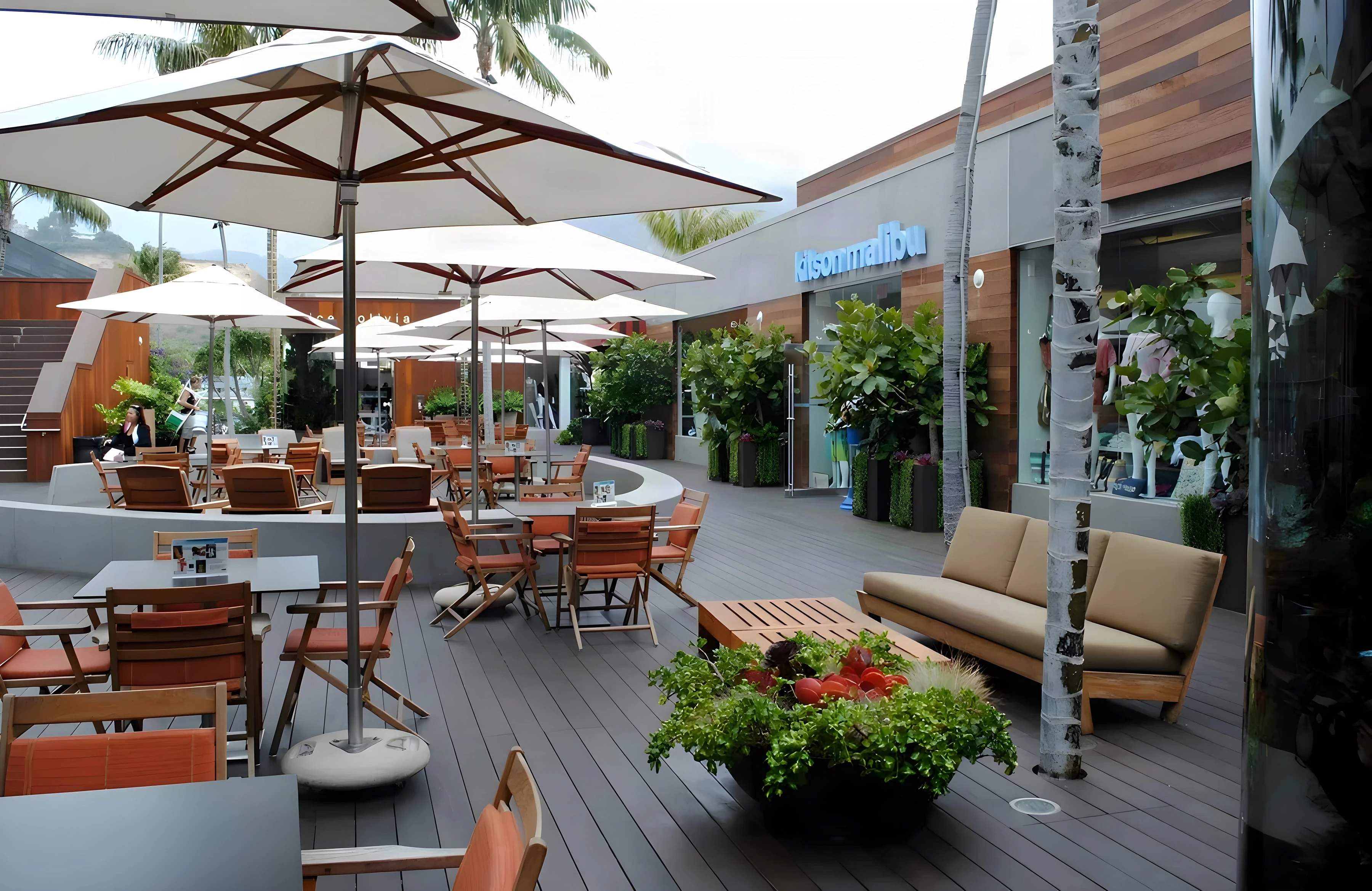 Café courtyard at Malibu Lumber Yard with white umbrellas, teak sofas and flower planters