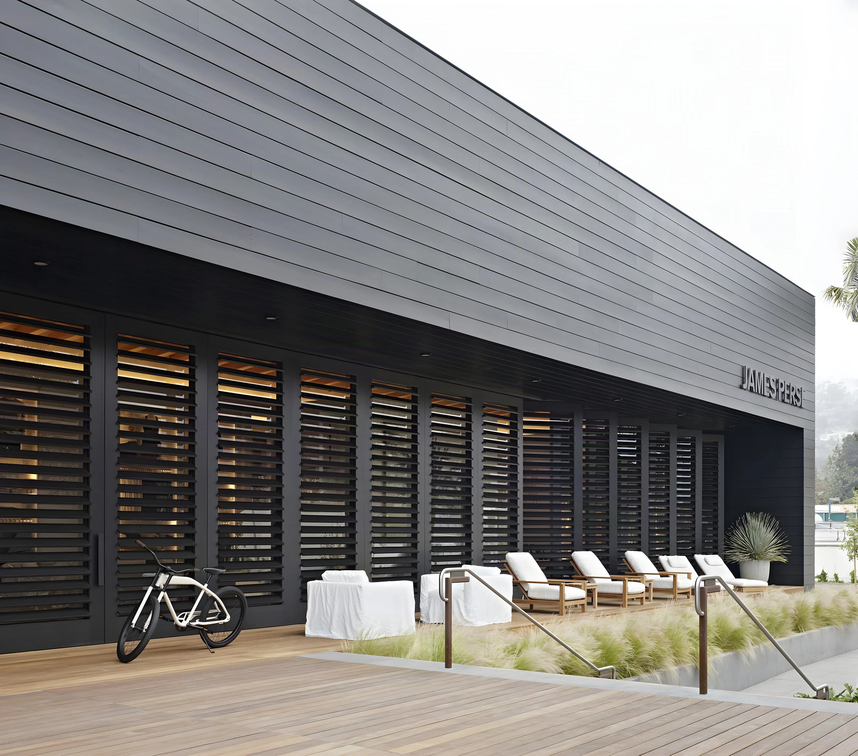 Black louvered facade of the Malibu Lumber Yard pavilion above a timber deck and loungers