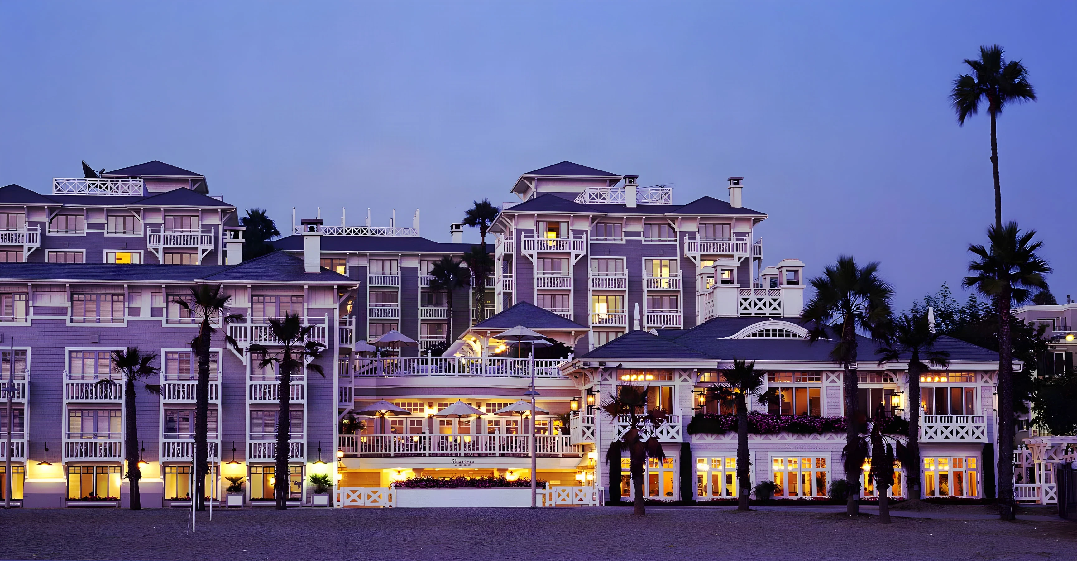 Shutters on the Beach facade lit at dusk behind palms along the beach path