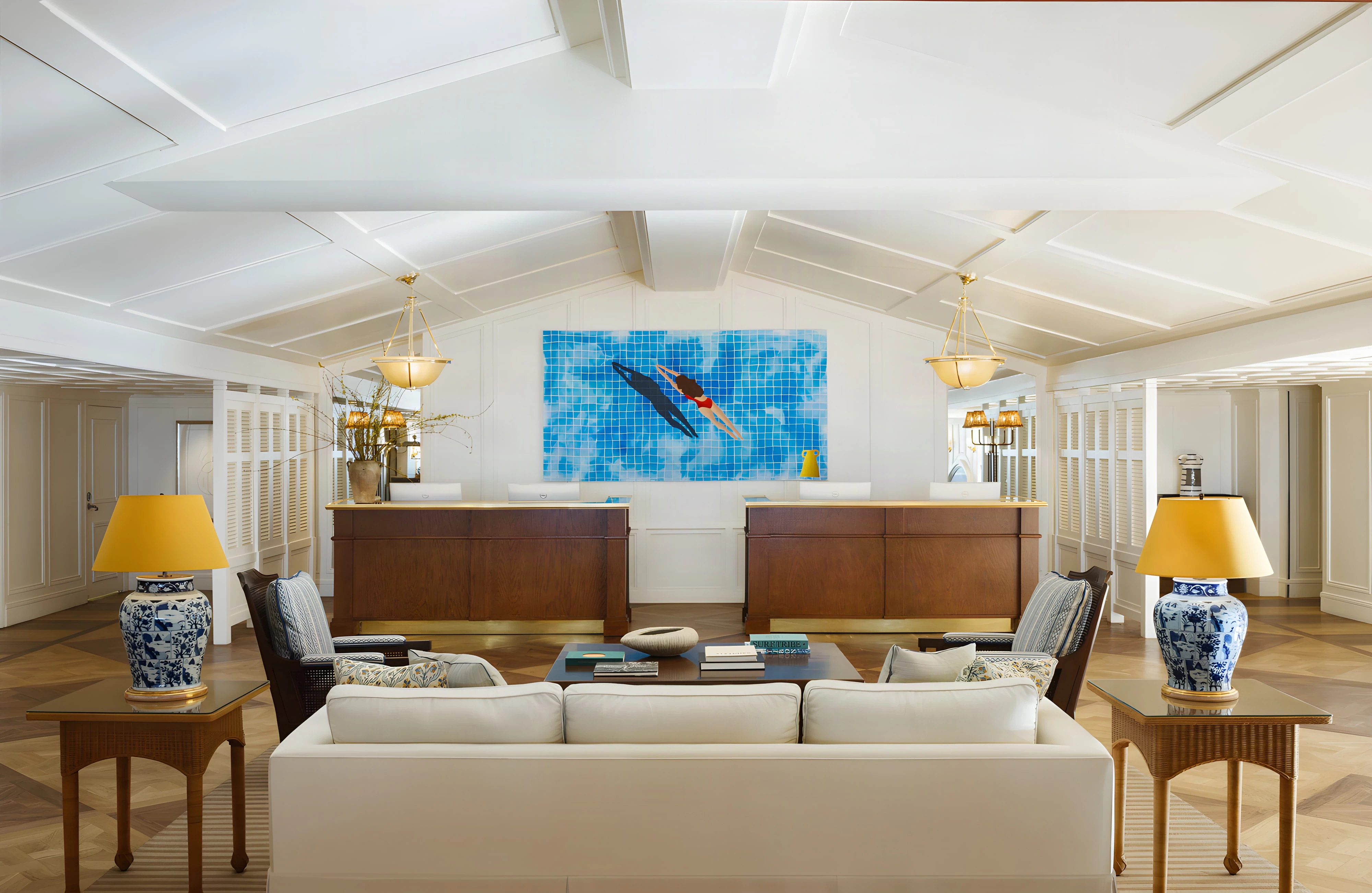 Shutters on the Beach lobby with twin wood reception desks, a swimmer artwork and blue-and-white lamps