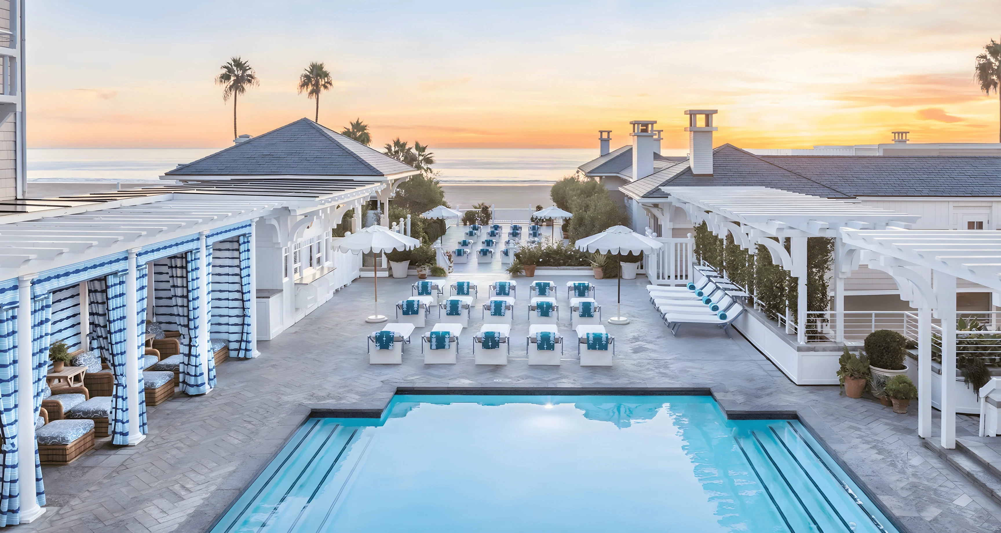 Shutters on the Beach pool deck and striped cabanas at sunset above the sand