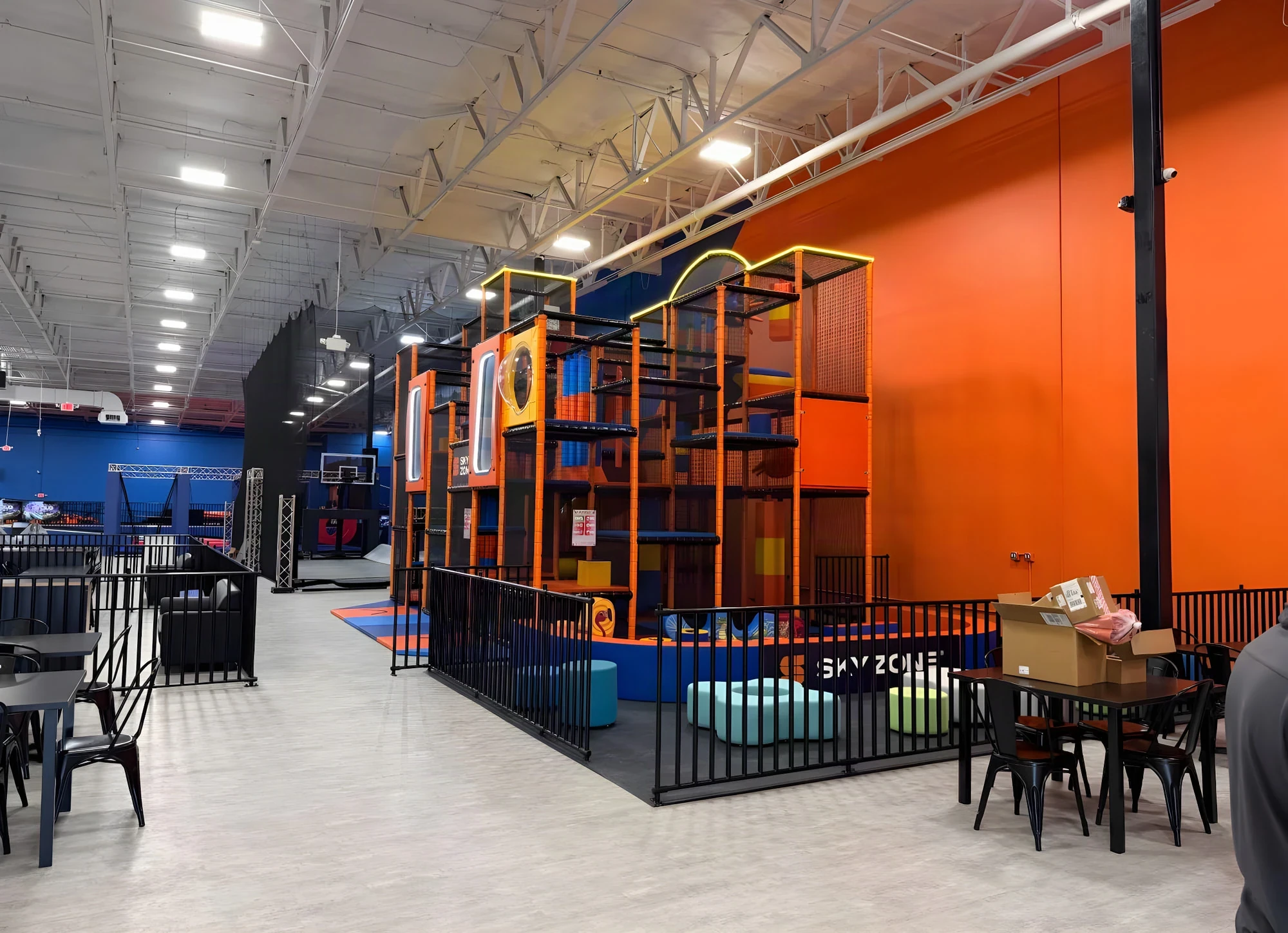 Orange and yellow climbing structure behind a black safety fence at Sky Zone Frisco
