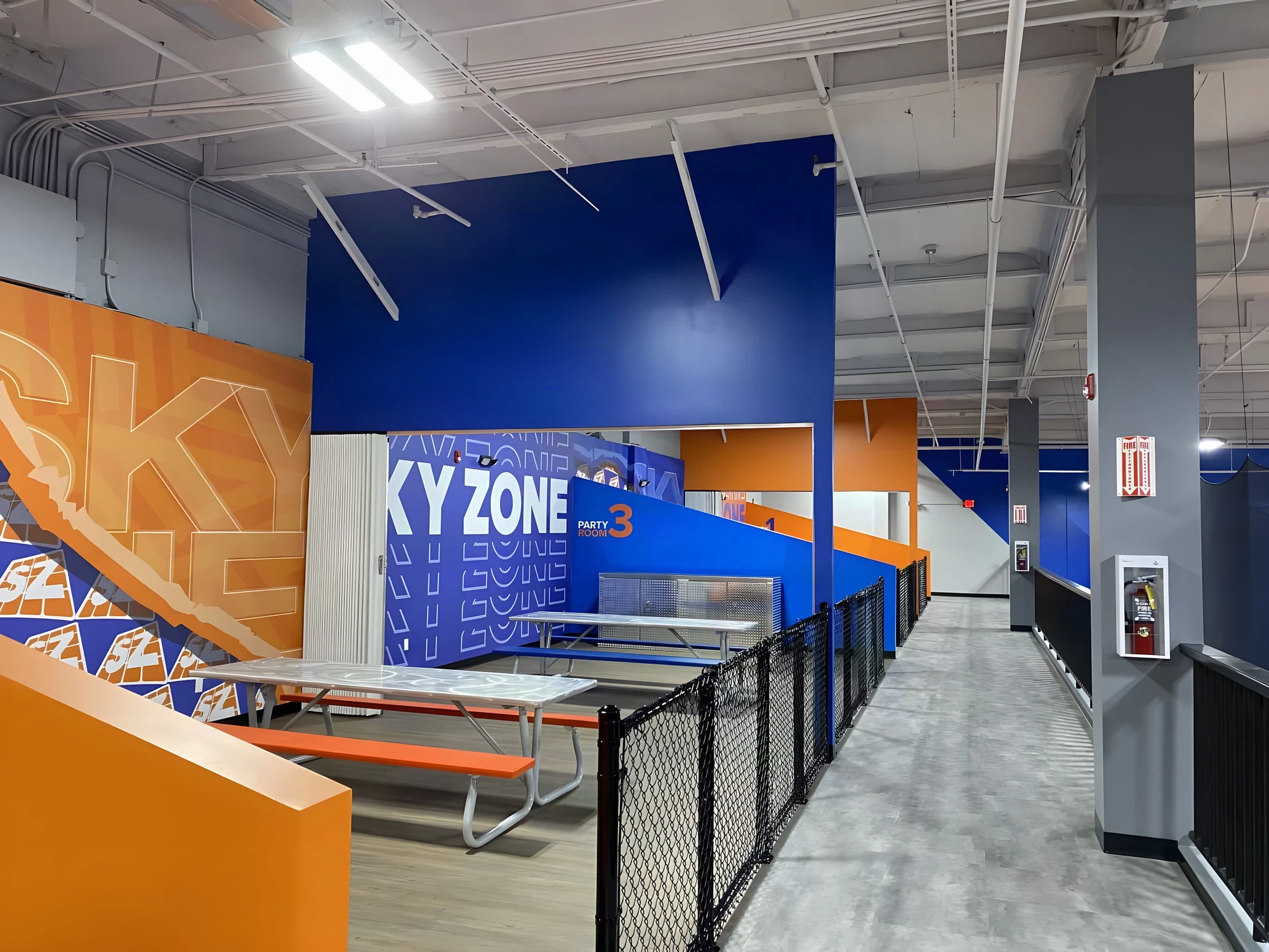 Party room tables beside a large Sky Zone mural wall and a caged walkway