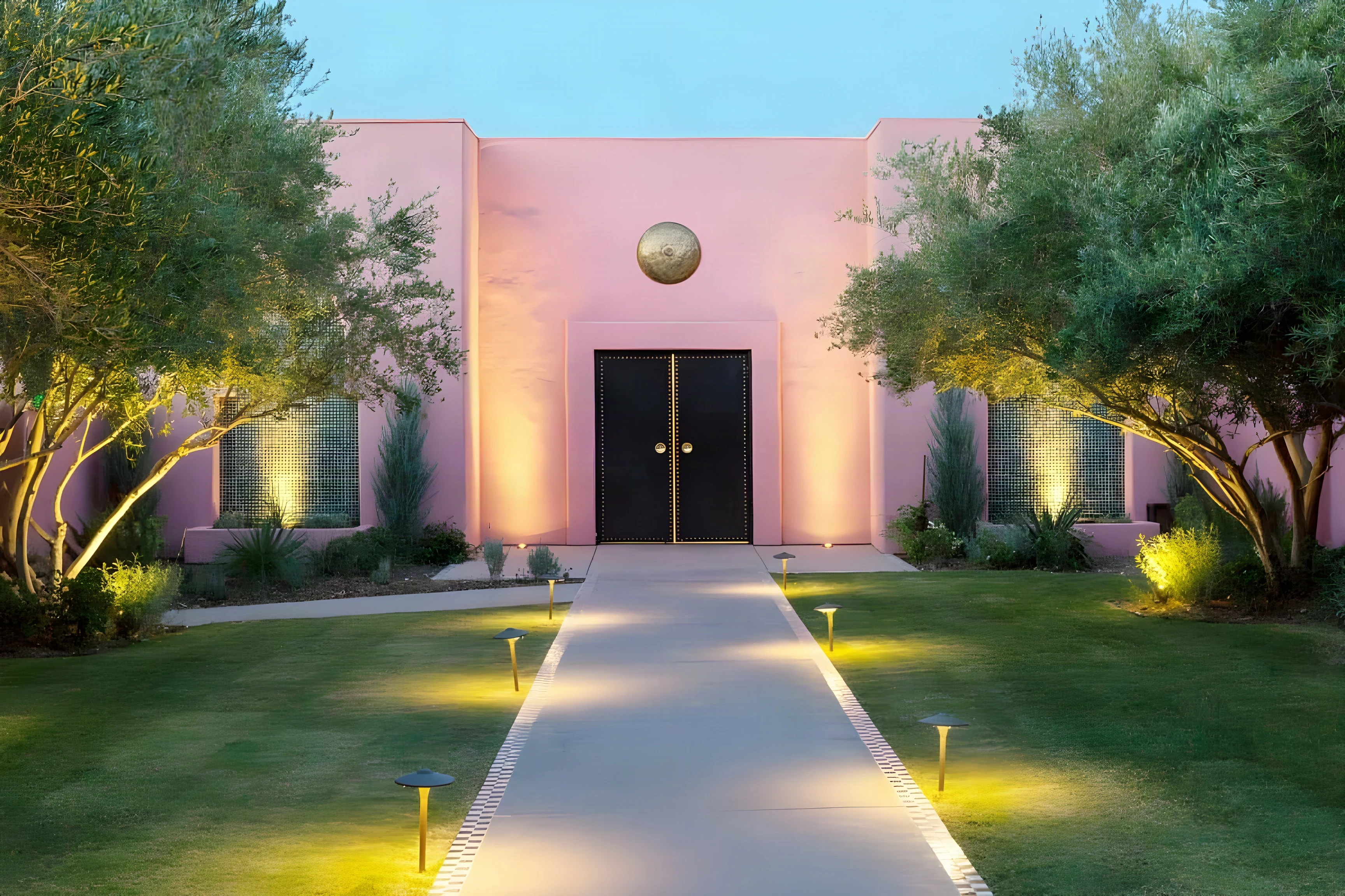 Pink stucco entrance of The Spa at Indian Wells at dusk, with uplit olive trees along the garden path
