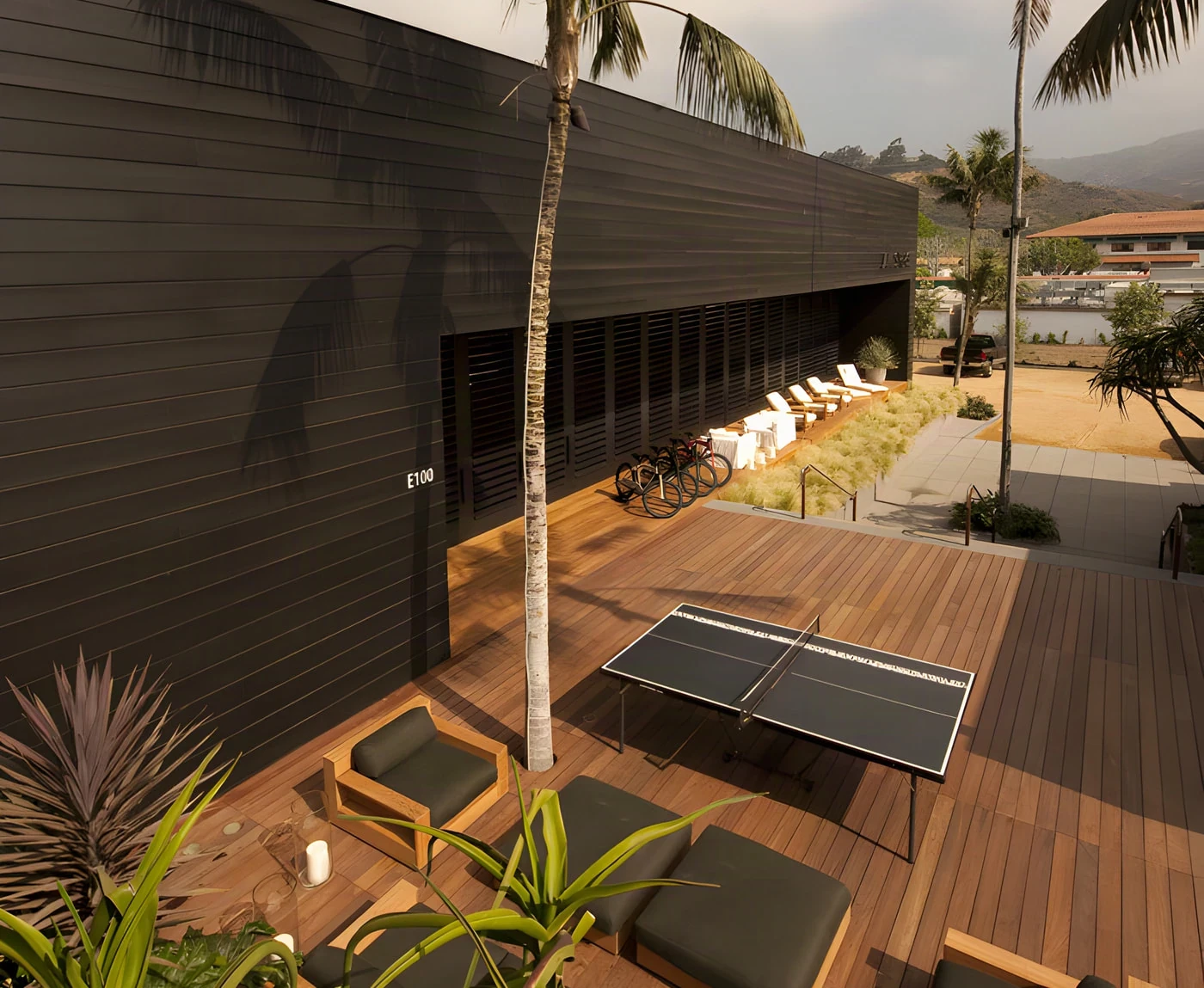 Black timber-clad pavilion and palm-shaded ipe deck with lounge seating at Malibu Lumber Yard